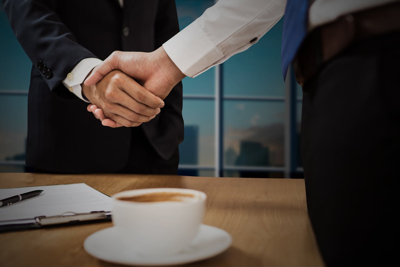 Mastering the First Impression: Your intriguing post title goes here Two professionals shaking hands across a desk with cityscape in the background.