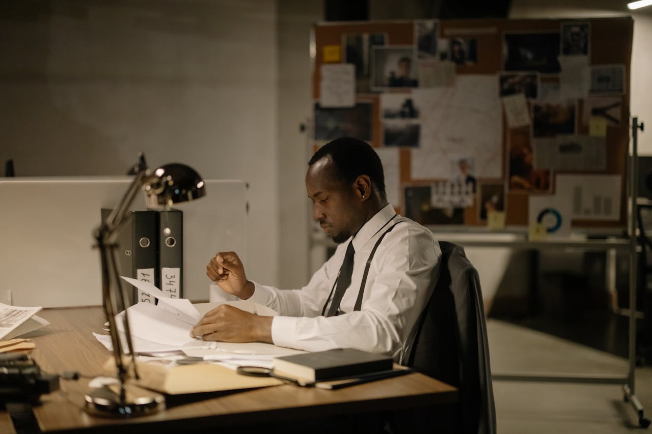 Man in office reviewing documents under desk lamp, late hours.